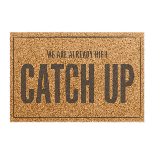Top view of the We Are Already High Catch Up coir doormat, dark lettering inside a thin border on natural tan fiber