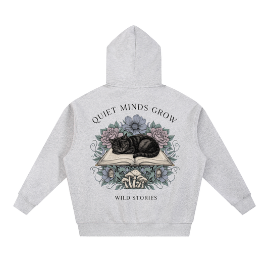 Unisex oversized boxy fleece hoodie with a sleeping black cat on an open book among flowers, Quiet Minds Grow, Wild Stories back print