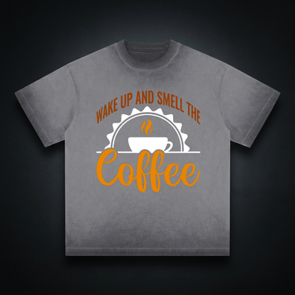 Washed gray reverse dye loose t-shirt with a rust brown Wake up and smell the coffee design with a white coffee cup and orange cursive Coffee on the front shown against a dark studio backdrop
