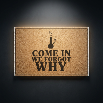 Come In We Forgot Why coir doormat with dark lettering on natural tan coir, shown on a dark studio backdrop