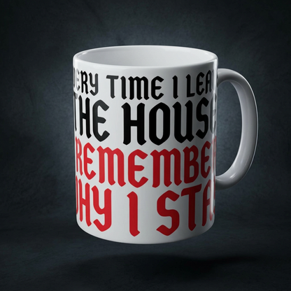 Funny coffee mug printed with "EVERY TIME I LEAVE THE HOUSE I REMEMBER WHY I STAY", shown on a dark studio background
