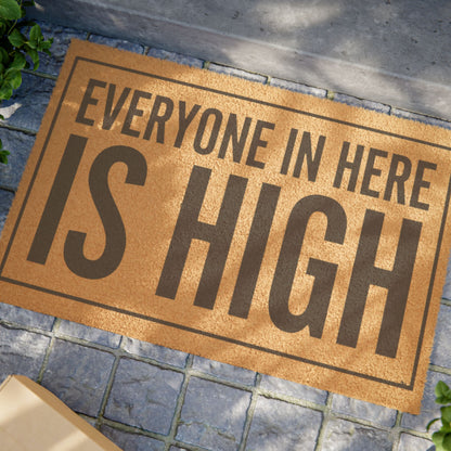 Close view of the Everyone in Here Is High coir doormat on a stone patio in dappled sunlight