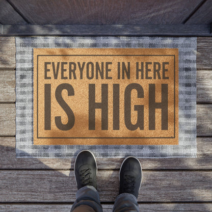 Everyone in Here Is High coir doormat on a wooden porch seen from above with a pair of shoes at the edge