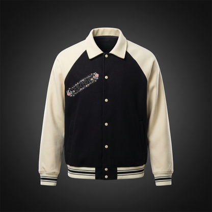 Baseball jacket with a black body and cream sleeves and a small diagonal strip of pink flowers and FAFO lettering on the chest, shown against a dark studio backdrop
