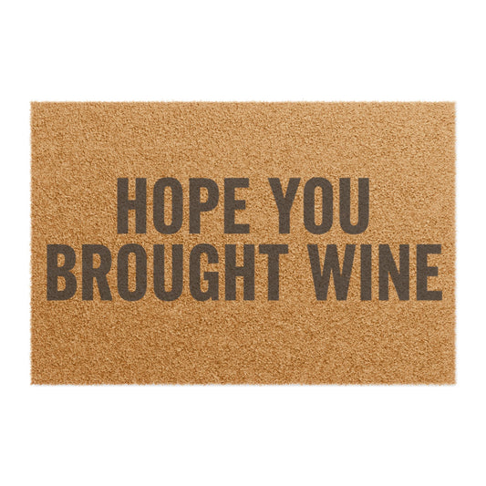 Top view of the Hope You Brought Wine coir doormat, two lines of dark lettering on natural tan fiber with no border