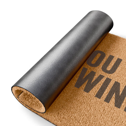Rolled-up corner of the Hope You Brought Wine coir doormat showing the black vinyl backing