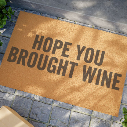 Close view of the Hope You Brought Wine coir doormat on a stone patio in dappled sunlight