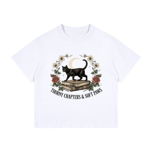 Kids’ loose-fit drop-shoulder tee with a black cat walking over old books under a crescent moon, Thorny Chapters & Soft Paws front print