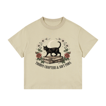 Kids’ loose-fit drop-shoulder tee with a black cat walking over old books under a crescent moon, Thorny Chapters & Soft Paws front print