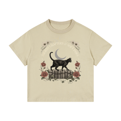 Kids’ loose-fit drop-shoulder tee with a black cat walking over old books under a crescent moon, Thorny Chapters & Soft Paws front print
