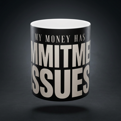 Funny coffee mug printed with "MY MONEY HAS COMMITMENT ISSUES", shown on a dark studio background
