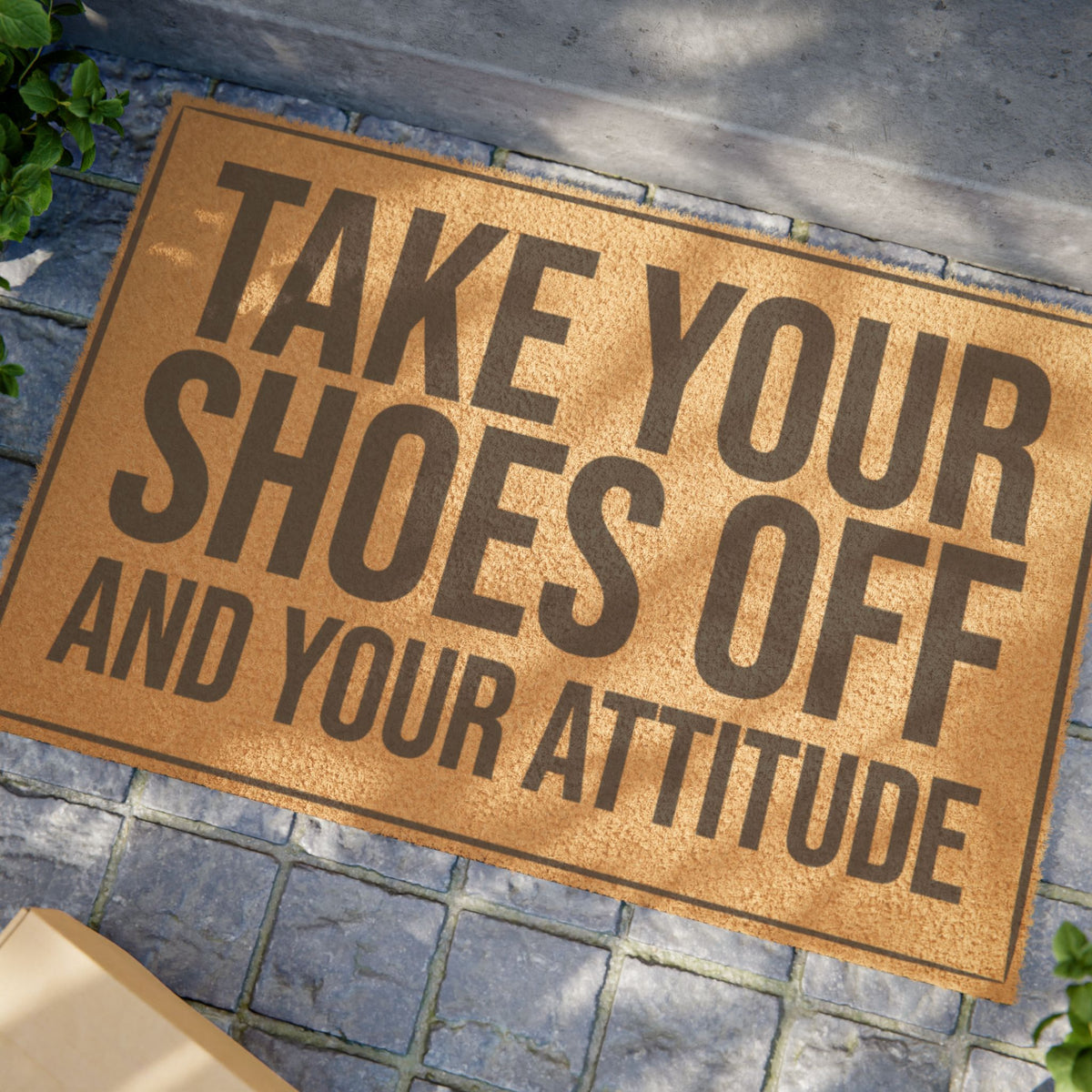 Close view of the Take Your Shoes Off and Your Attitude coir doormat on a stone patio in dappled sunlight