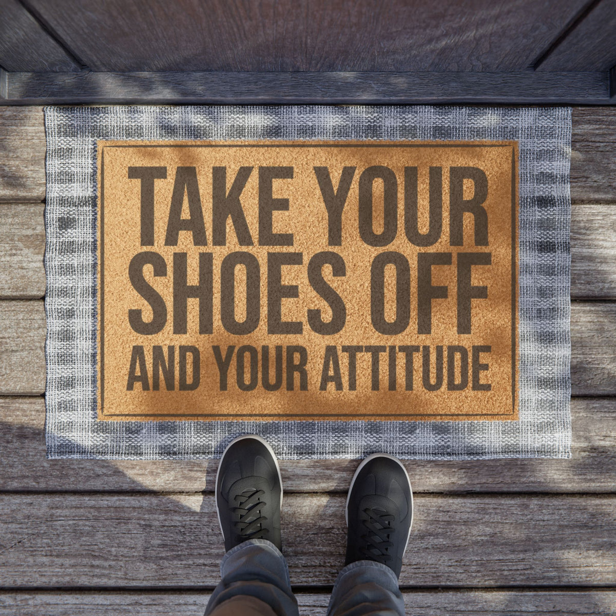 Take Your Shoes Off and Your Attitude coir doormat on a wooden porch seen from above with a pair of shoes at the edge