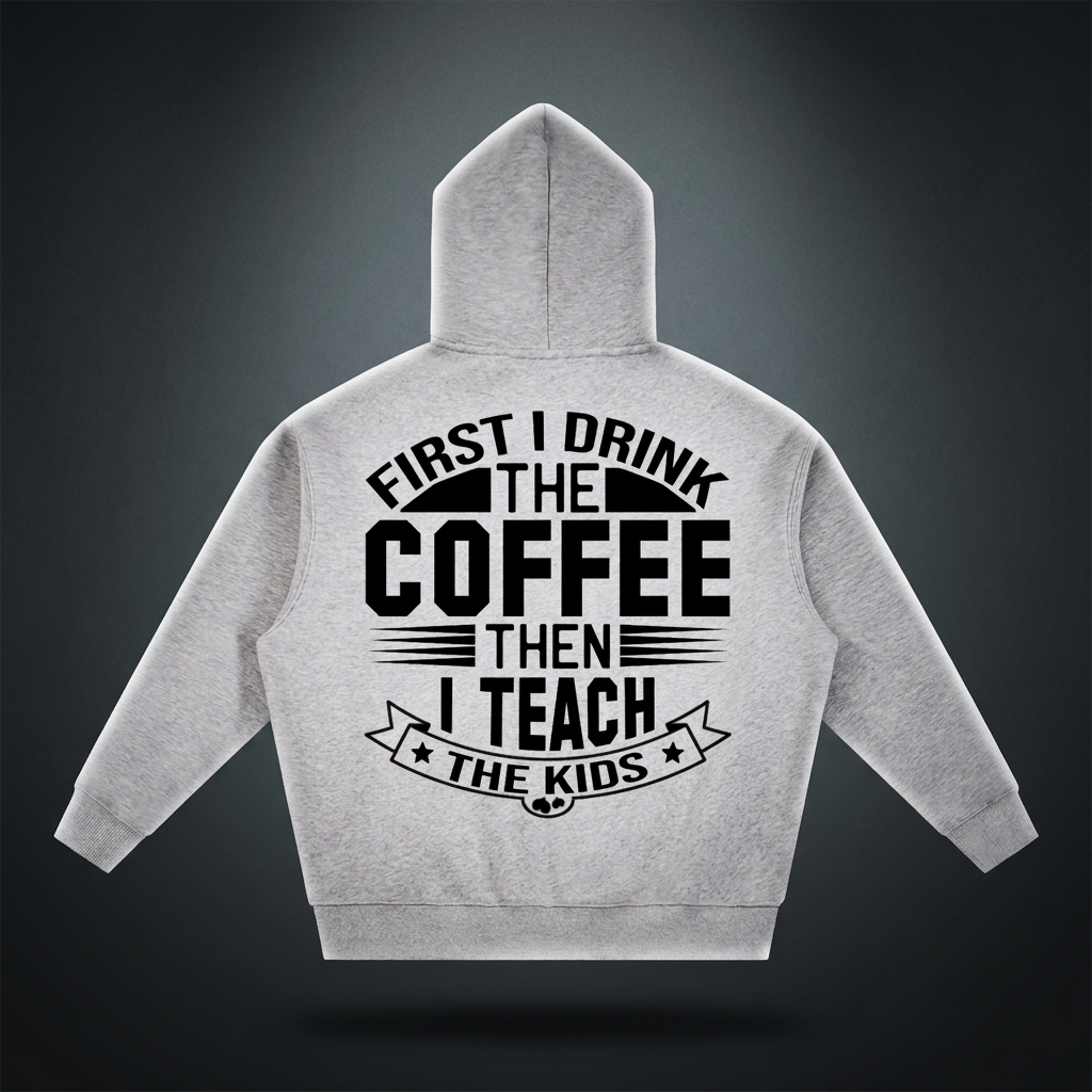 Heather gray oversized boxy fleece hoodie with black First I drink the coffee then I teach the kids lettering with a star ribbon banner on the back shown against a dark studio backdrop