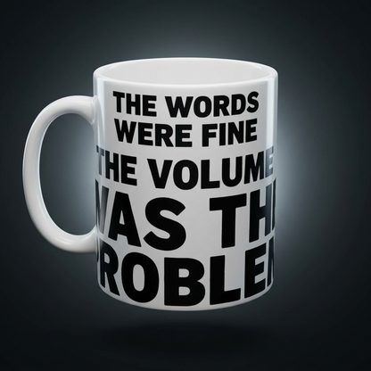 Funny coffee mug printed with "THE WORDS WERE FINE THE VOLUME WAS THE PROBLEM", shown on a dark studio background