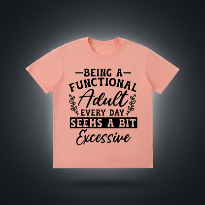 Peach T-shirt reading “Being a functional adult every day seems a bit excessive,” displayed against a dark charcoal studio background.