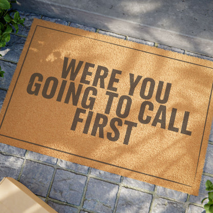 Close view of the Were You Going to Call First coir doormat on a stone patio in dappled sunlight