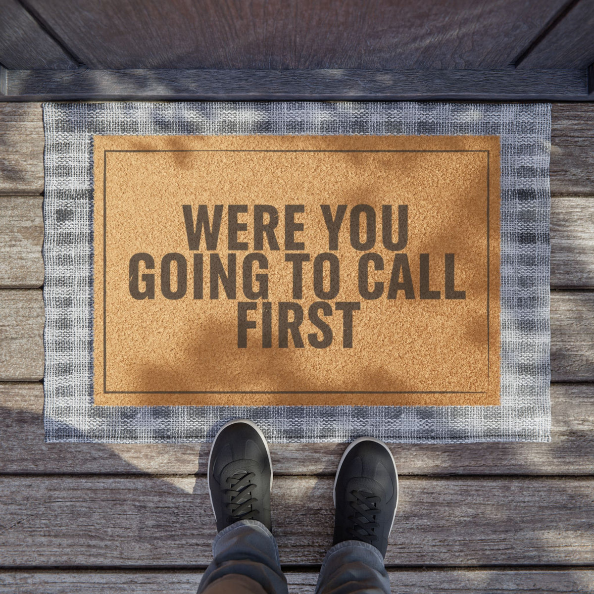 Were You Going to Call First coir doormat on a wooden porch seen from above with a pair of shoes at the edge
