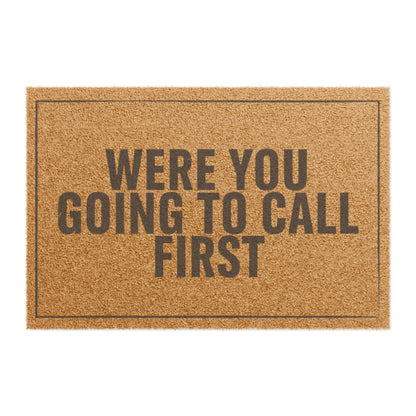 Top view of the Were You Going to Call First coir doormat, dark lettering inside a thin border on natural tan fiber