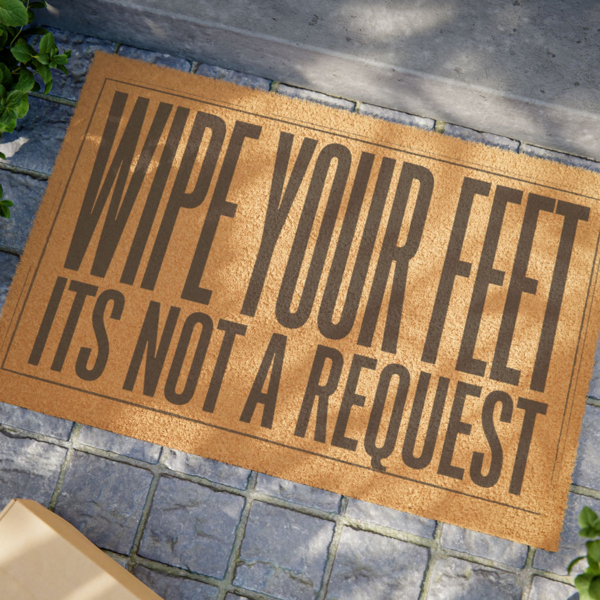 Close view of the Wipe Your Feet It's Not a Request coir doormat on a stone patio in dappled sunlight