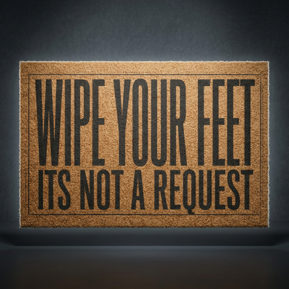Wipe Your Feet It's Not a Request coir doormat with dark lettering on natural tan coir, shown on a dark studio backdrop