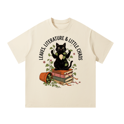 Unisex oversized heavyweight cotton tee with a black cat on books beside a tipped plant pot, Leaves, Literature & Little Chaos front print