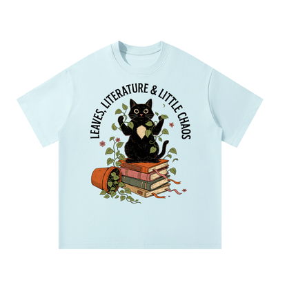 Unisex oversized heavyweight cotton tee with a black cat on books beside a tipped plant pot, Leaves, Literature & Little Chaos front print
