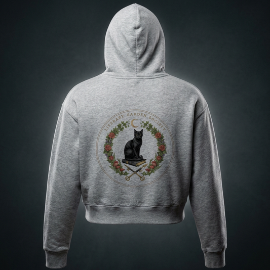Women’s Literary Garden Society Cropped Drop-Shoulder Hoodie in gray, back view with the black cat and roses crest, on a dark studio background
