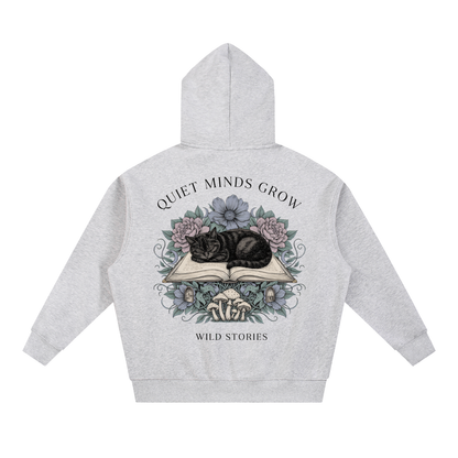 Unisex oversized boxy fleece hoodie with a sleeping black cat on an open book among flowers, Quiet Minds Grow, Wild Stories back print