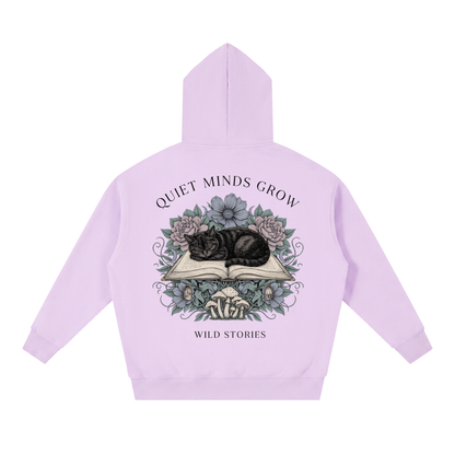 Unisex oversized boxy fleece hoodie with a sleeping black cat on an open book among flowers, Quiet Minds Grow, Wild Stories back print
