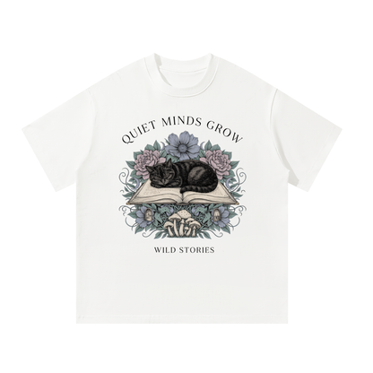 Unisex oversized heavyweight cotton tee with a sleeping black cat on an open book among flowers, Quiet Minds Grow, Wild Stories front print