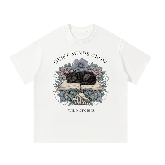 Unisex oversized heavyweight cotton tee with a sleeping black cat on an open book among flowers, Quiet Minds Grow, Wild Stories front print