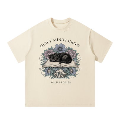 Unisex oversized heavyweight cotton tee with a sleeping black cat on an open book among flowers, Quiet Minds Grow, Wild Stories front print