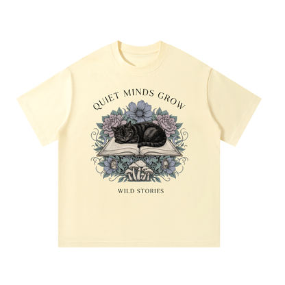Unisex oversized heavyweight cotton tee with a sleeping black cat on an open book among flowers, Quiet Minds Grow, Wild Stories front print