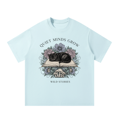 Unisex oversized heavyweight cotton tee with a sleeping black cat on an open book among flowers, Quiet Minds Grow, Wild Stories front print