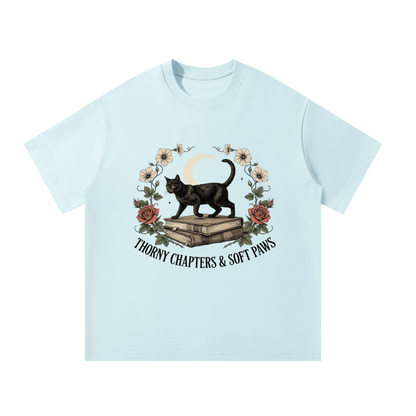 Unisex oversized heavyweight cotton tee with a black cat walking over old books under a crescent moon, Thorny Chapters & Soft Paws front print