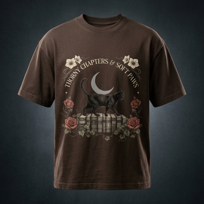 Unisex oversized heavyweight cotton tee with a black cat walking over old books under a crescent moon, Thorny Chapters & Soft Paws front print