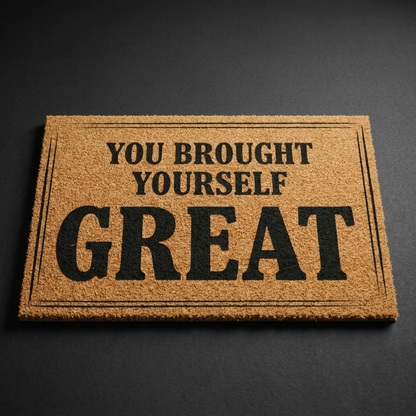 You Brought Yourself Great coir doormat with dark lettering on natural tan coir, shown at an angle on a dark studio backdrop