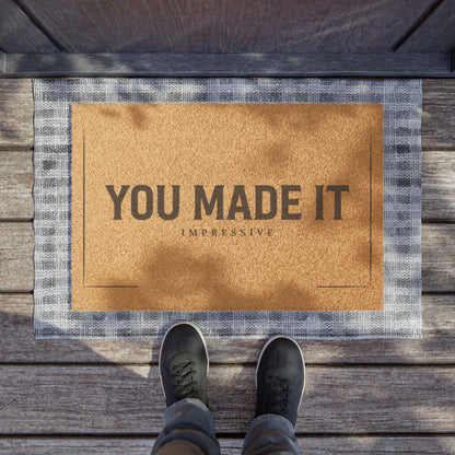 You Made It Impressive coir doormat on a wooden porch seen from above with a pair of shoes at the edge