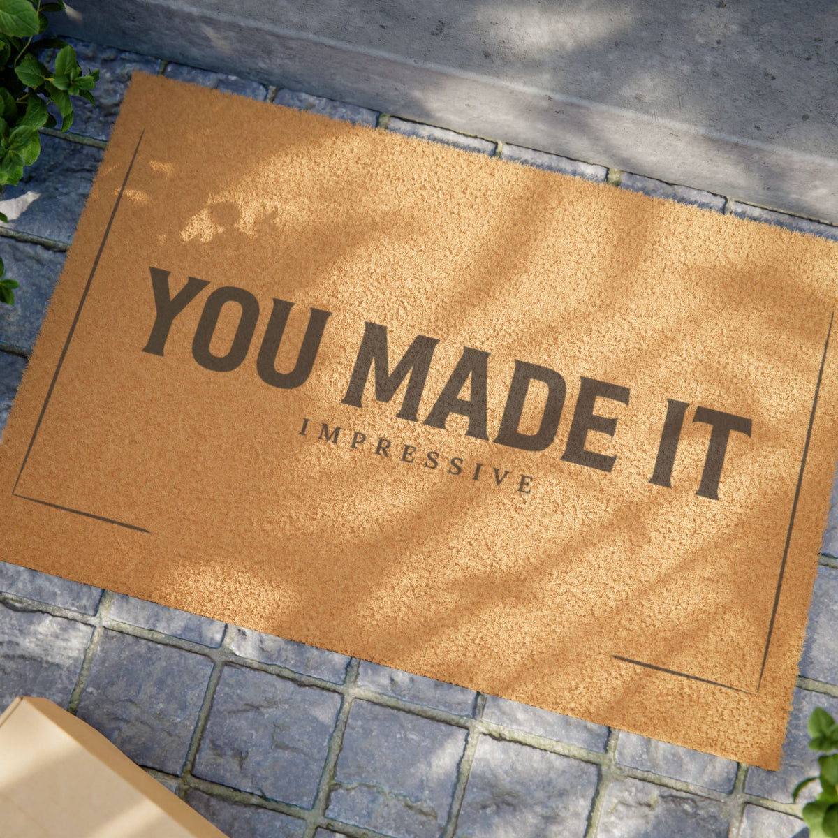 Close view of the You Made It Impressive coir doormat on a stone patio in dappled sunlight
