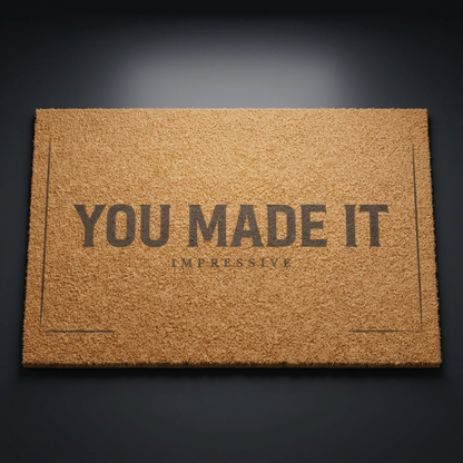 You Made It Impressive coir doormat with dark lettering on natural tan coir, shown at an angle on a dark studio backdrop